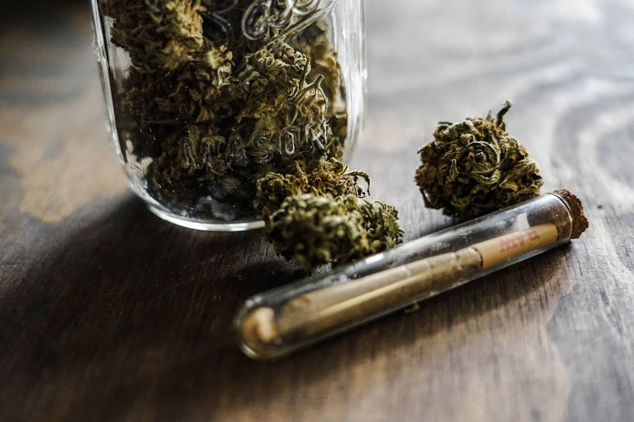 A detailed close-up of cannabis buds in a jar with a joint on a wooden surface.